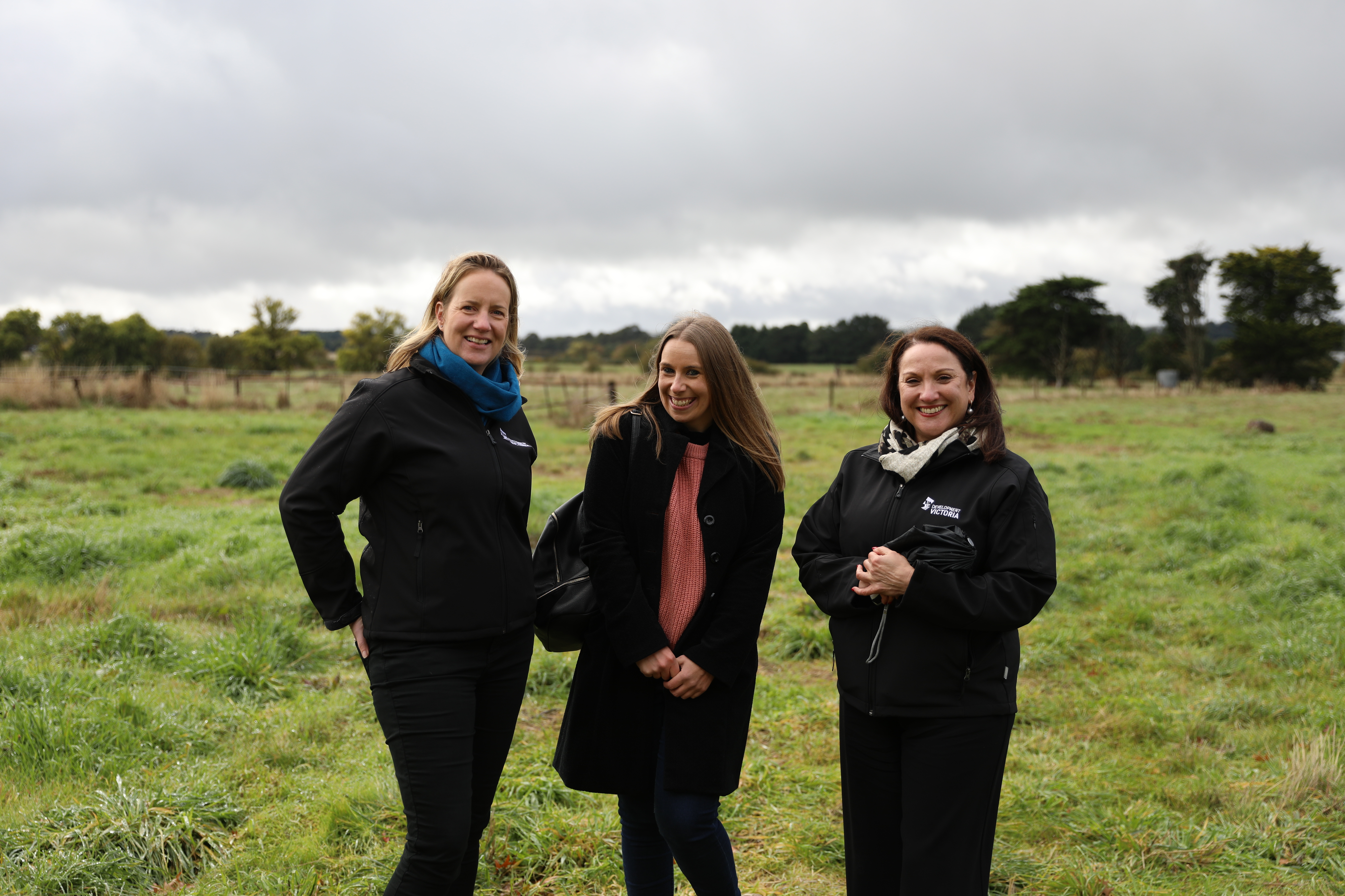 Three white women smiling to camera in a green field which is the future Miners Rest sporting facility