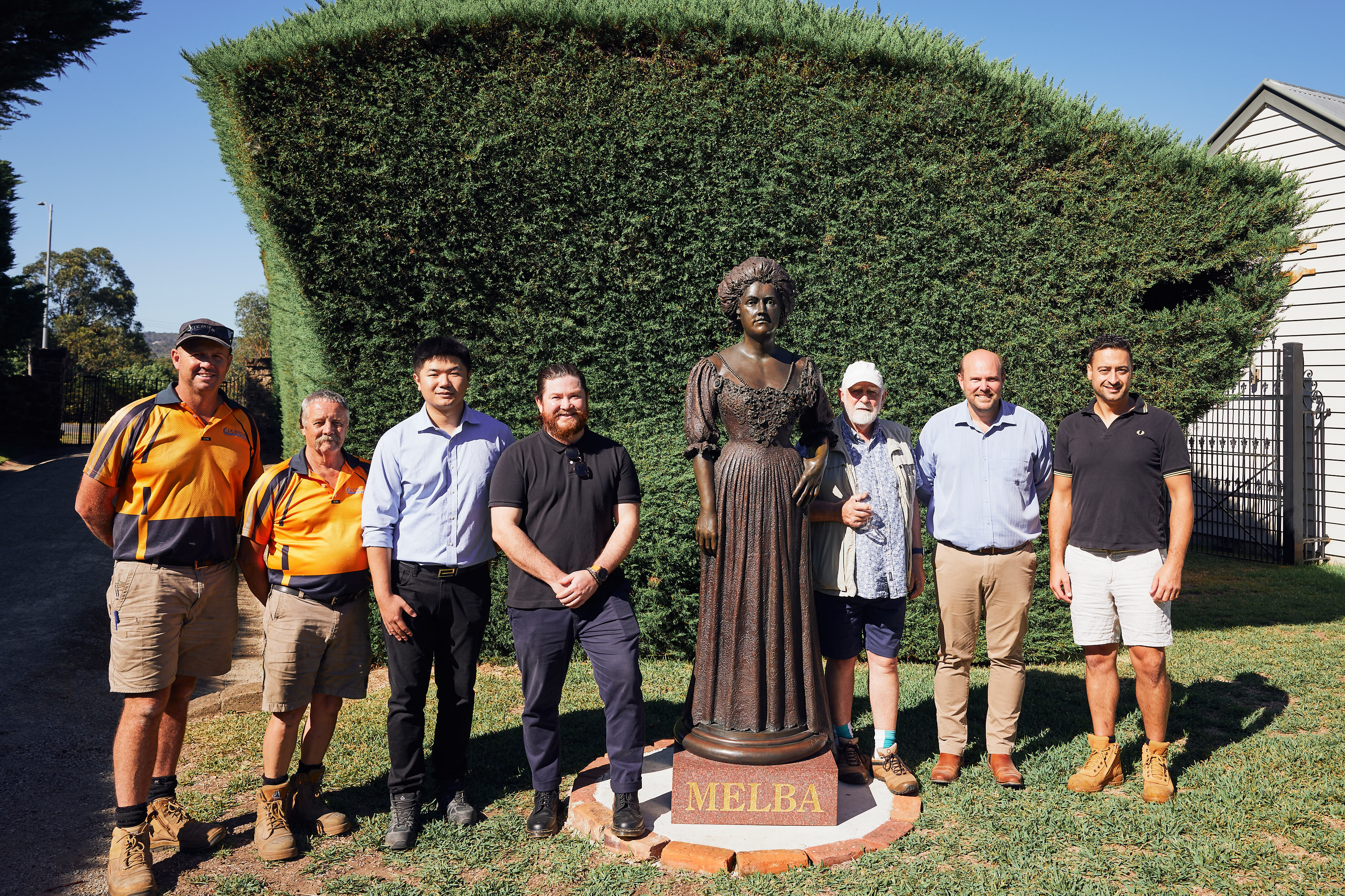 Seven men standing around a bronze statue of Dame Nellie Melba statue at Coombe Yarra Valley