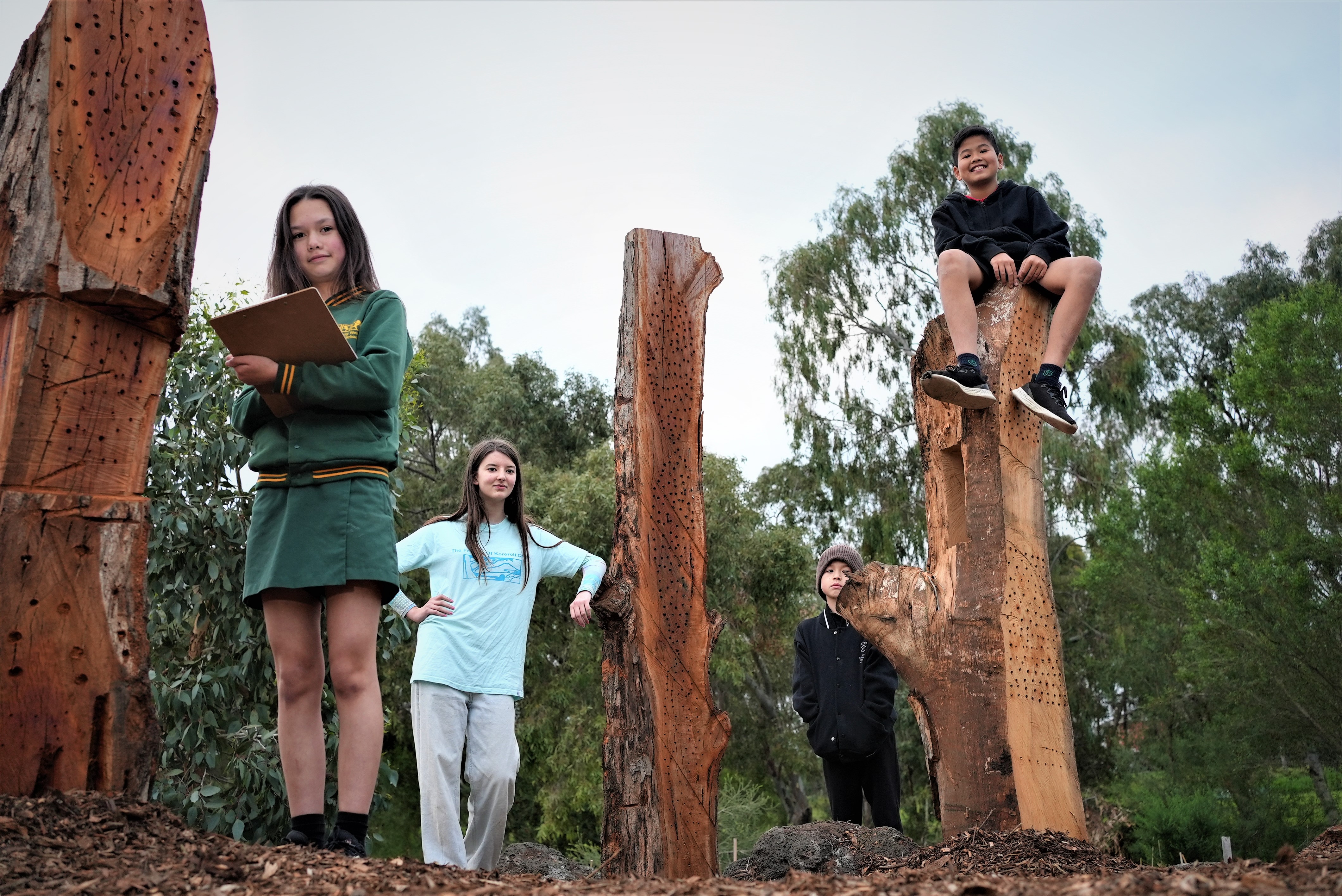 Four children standing with trees that have been turned into bug hotels