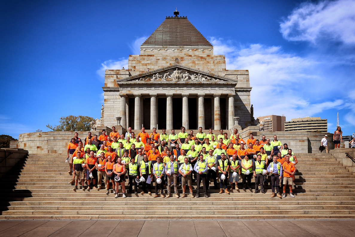 A group of men and women in yellow and orange high vis standing in front of the Shrine of Rememberance